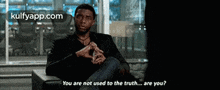 a man in a black shirt is sitting in a chair and talking to someone .