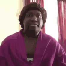 a man wearing a purple robe and a hat is looking at the camera .