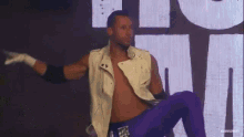 a man in a white vest and purple pants is dancing in front of a large screen that says musclenet