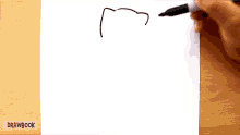 a person is drawing a cat on a piece of white paper