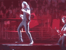 a man stands on a stage in front of a crowd with a 1d sign behind him