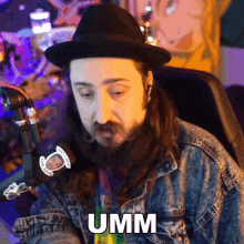 a man with a beard wearing a hat and a denim jacket has the word umm on his chest