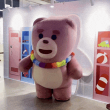 a pink teddy bear with a rainbow scarf around his neck is standing in front of a wall with a picture of a beach ball