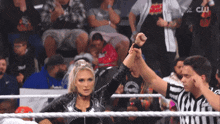 a woman in a wrestling ring holds a referee 's hand in front of a crowd