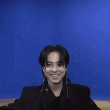 a man with long hair is waving his hand in front of a blue background