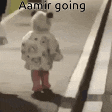 a baby is walking down a sidewalk with the words `` aamir going '' written on the bottom .