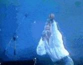 a man in a white shirt is singing into a microphone on stage