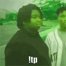 a man in a black jacket is standing next to another man in a white jersey and says tp .