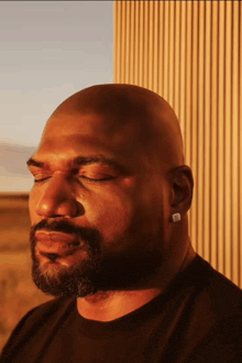 a bald man with a beard and ear rings looks down with his eyes closed