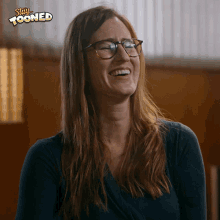 a woman wearing glasses is smiling with a stay tooned sticker behind her