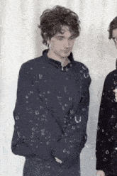 a young man in a black jacket is standing in front of a white curtain with bubbles coming out of it .