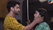a man in a yellow shirt is touching the face of a woman