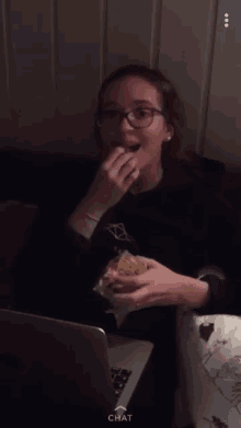 a girl is sitting in front of a laptop and eating a snack