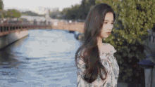 a woman with long hair is standing next to a body of water .