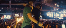 a man in a green shirt is hugging another man in front of a crowd at a concert
