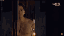 a shirtless man is standing in front of a window with a candle in it .