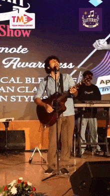 a man singing into a microphone while playing a guitar at a glitterati show