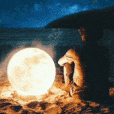 a person is sitting on the beach looking at the moon