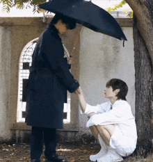 a man in a black coat is holding the hand of another man in a white shirt under an umbrella