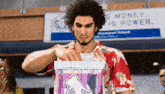a man in a hawaiian shirt holds a box in front of a sign that says ' money is power '