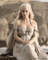 a woman in a white dress is sitting on a wooden plank .