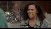 a woman with curly hair says i 'm pregnant in front of a row of bikes