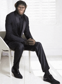 a man in a suit is sitting on a chair with his hands folded