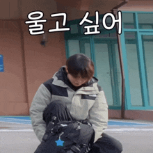 a man in a jacket is kneeling down in front of a building with korean writing on it