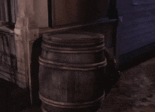 a man in a cowboy hat is behind a wooden barrel