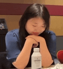 a woman is sitting at a table with her eyes closed and a bottle of unifort in front of her .