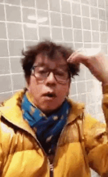 a man wearing glasses and a yellow jacket is standing in front of a wall .