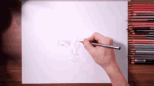 a person is drawing on a piece of paper with colored pencils on the table