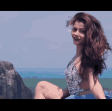 a woman in a swimsuit is sitting on a rock near the ocean .