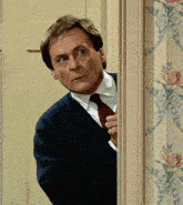 a man in a suit and tie is peeking through a doorway