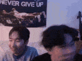 a couple of men are sitting in front of a poster that says `` never give up '' .