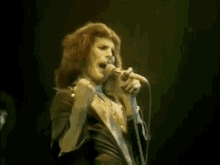 queen freddie mercury is singing into a microphone on stage .