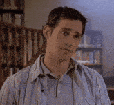 a man in a striped shirt is standing in front of a bookshelf and stairs .