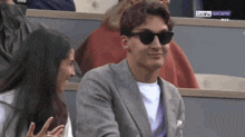 a man wearing sunglasses sits next to a woman in a stadium watching a sports game