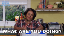 a woman in a plaid shirt is standing in a kitchen holding a bag of ice and asking what are you doing