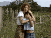 a woman is hugging a boy in a field .