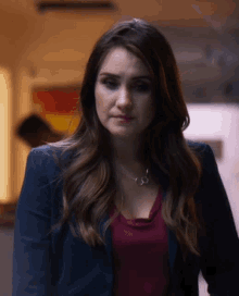 a woman wearing a blue jacket and a red top is looking at the camera