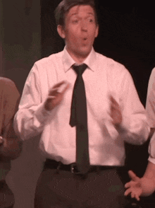 a man in a white shirt and tie is standing on a stage with his hands outstretched .