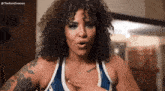 a woman with curly hair is wearing a blue and white tank top with a tattoo on her arm