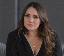 a woman wearing a black jacket and a gold necklace has a coin pendant around her neck