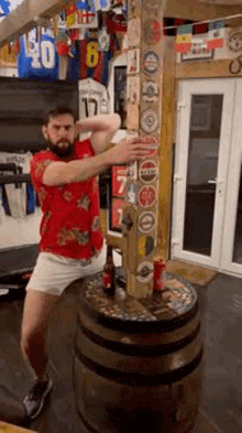 a man in a red shirt is standing on a barrel with a bottle of beer .