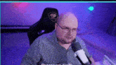 a man wearing glasses is sitting in front of a microphone .