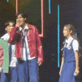 a man in a red jacket is talking into a microphone while standing next to a girl in a blue uniform