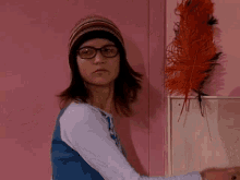 a young girl wearing glasses and a hat is standing in front of a pink wall .
