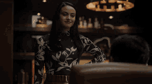 a woman in a black and white floral top is standing in a dark room