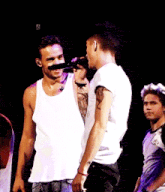 a man in a white tank top is singing into a microphone on stage